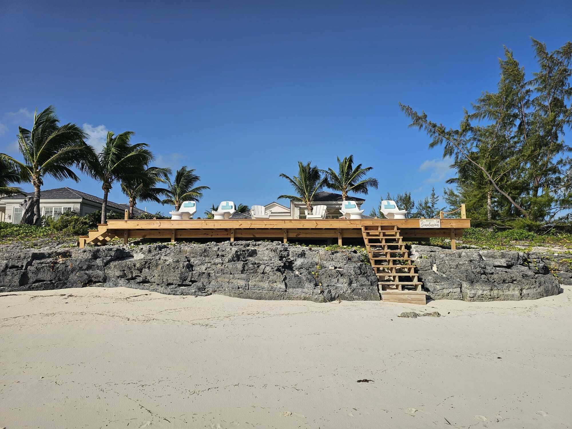 A beachside wooden structure with a staircase leading to a deck with lounge chairs.