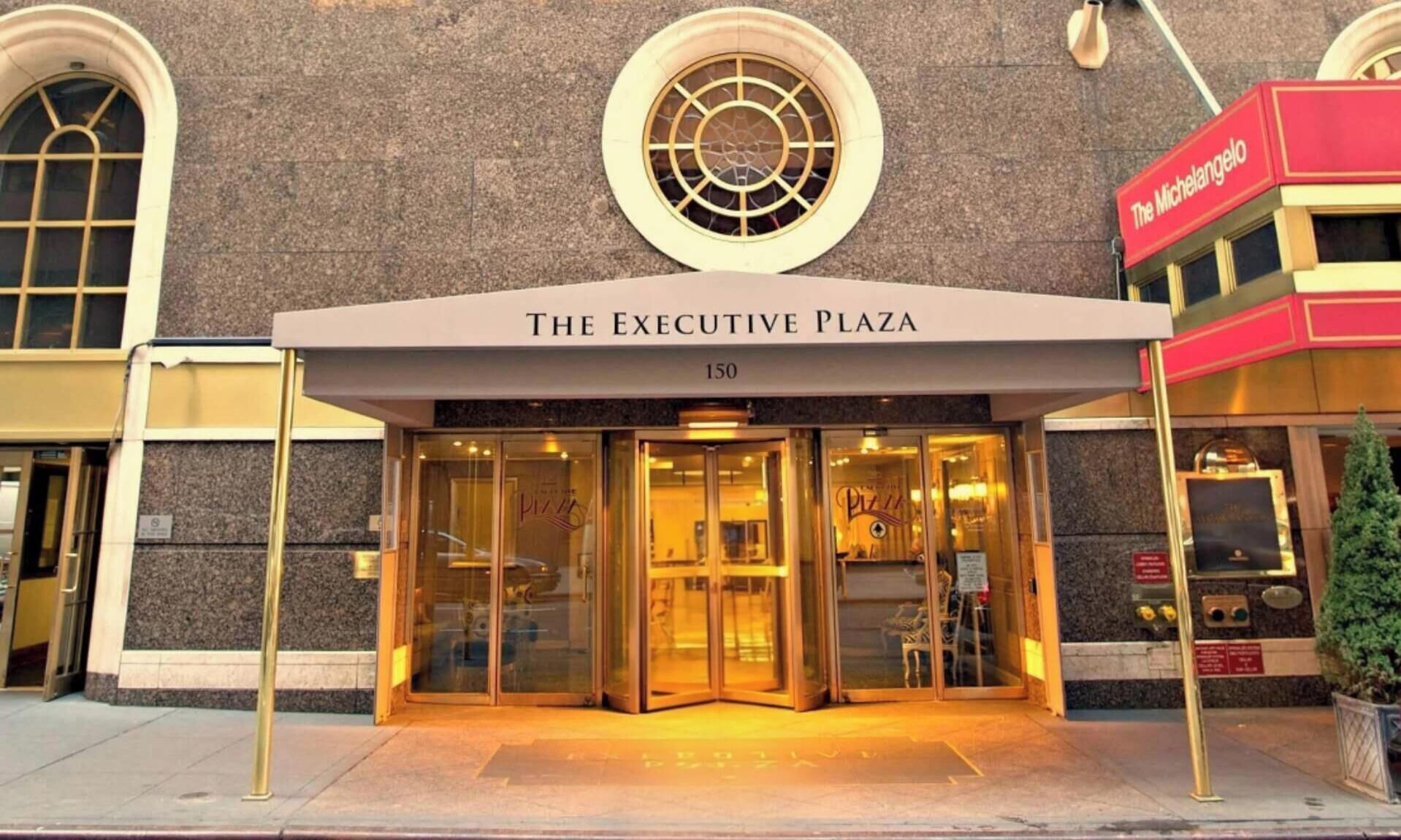 The entrance to The Executive Plaza, featuring a glass door entrance, a prominent circular window above the entrance, and a red awning with the name 'The Michelangelo' to the right.