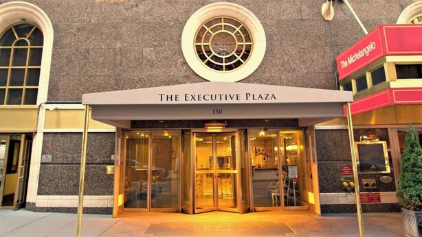 The entrance to The Executive Plaza, featuring a glass door entrance, a prominent circular window above the entrance, and a red awning with the name 'The Michelangelo' to the right.