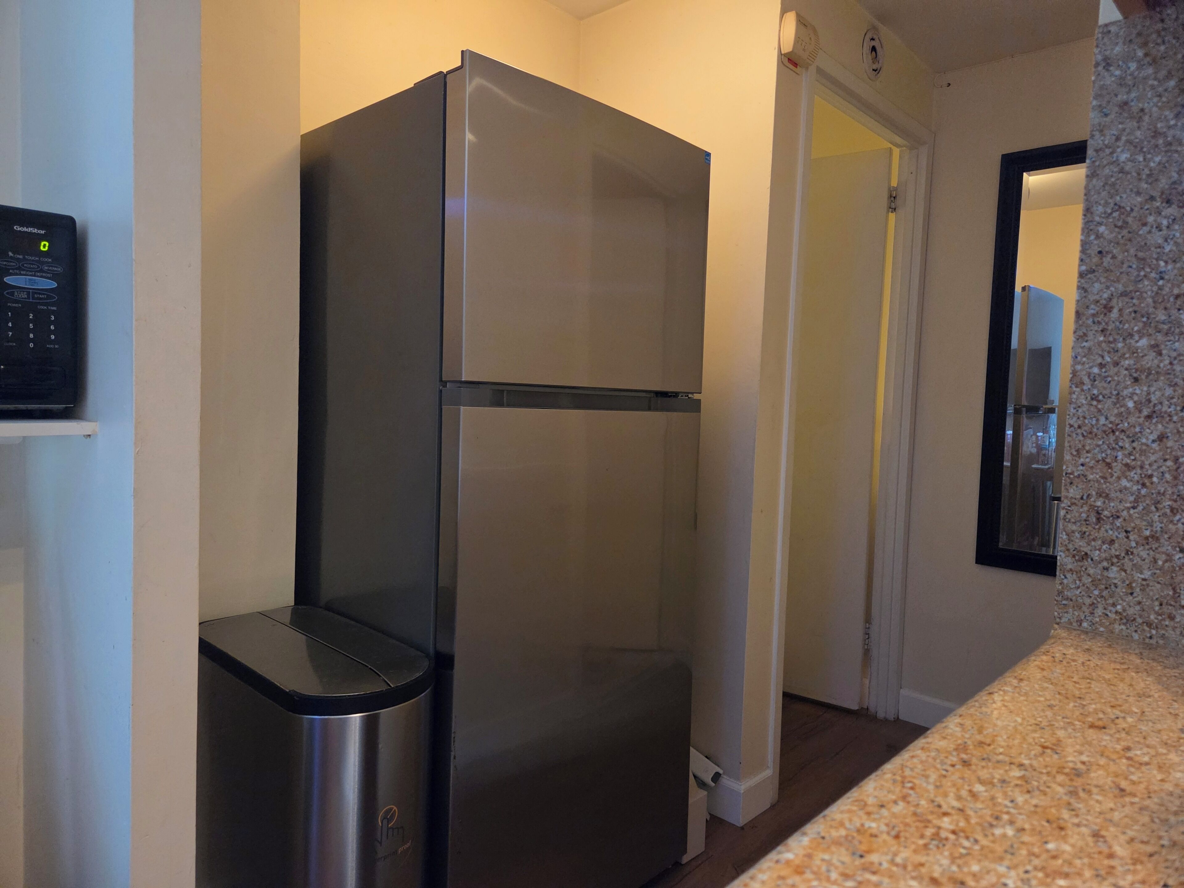 A stainless steel refrigerator in a kitchen with a granite countertop and a microwave on the left.