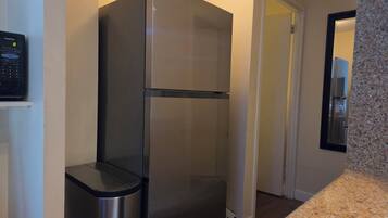 A stainless steel refrigerator in a kitchen with a granite countertop and a microwave on the left.