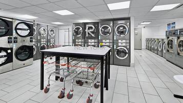 A laundromat with multiple washing machines, a table with a basket, and a tiled floor.