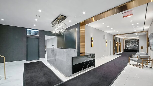 A modern reception area with a marble reception desk, a chandelier, and a carpeted floor.