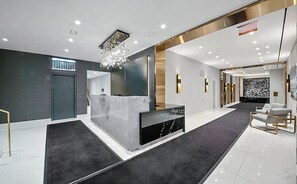 A modern reception area with a marble reception desk, a chandelier, and a carpeted floor.