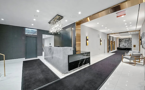 A modern reception area with a marble reception desk, a chandelier, and a carpeted floor.