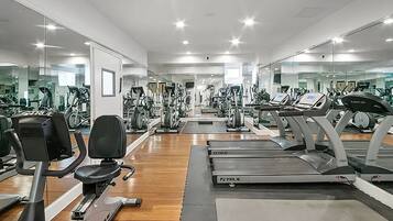 A gym with multiple exercise machines, including treadmills and stationary bikes, arranged in rows.