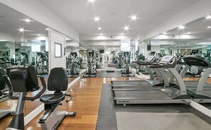 A gym with multiple exercise machines, including treadmills and stationary bikes, arranged in rows.