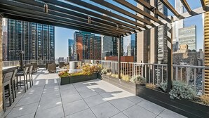 A rooftop terrace with a pergola, seating area, and a view of surrounding high-rise buildings.