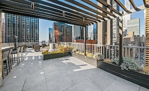 A rooftop terrace with a pergola, seating area, and a view of surrounding high-rise buildings.