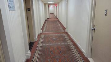 A hotel hallway with a patterned carpet, white walls, and doors on both sides.