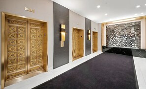 A hallway with a black carpet, a wall-mounted light fixture, and a mosaic tile wall.