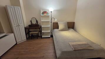 Une chambre à coucher comprenant un lit, un bureau avec une chaise, une armoire et une étagère avec une lampe.