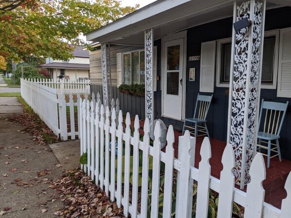 A house with a white picket fence, a porch with two chairs, and a mailbox.