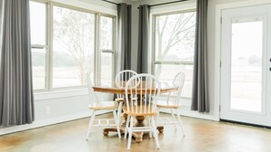 Un comedor con una mesa redonda y cuatro sillas, ventanas grandes con cortinas y una puerta.