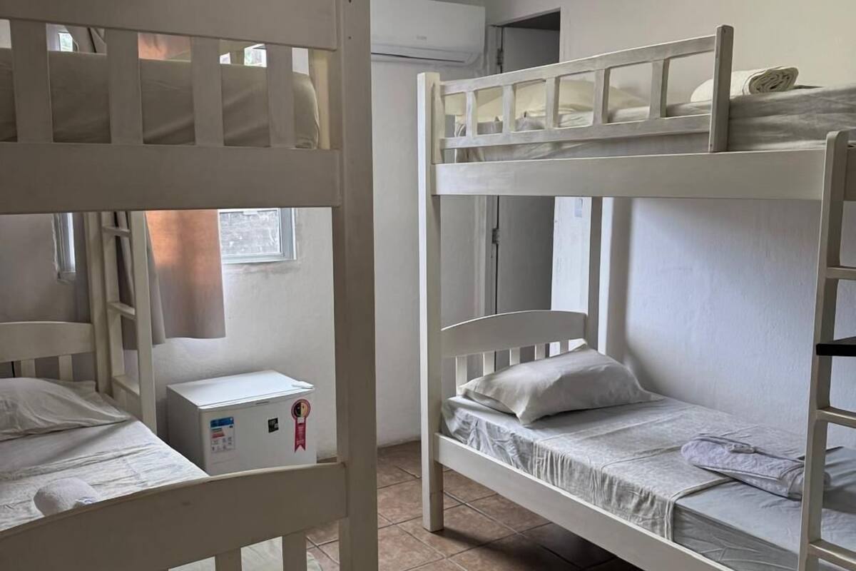 A dormitory room with two bunk beds, a small bedside table, and a window.