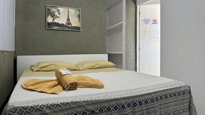 A bed with a patterned bedspread, a rolled-up towel, and a pillow. There is a framed picture of the Eiffel Tower on the wall. - Casa Aeroporto Pousada (Recife)