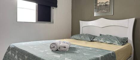 A single bed with a geometric patterned bedspread, a white headboard, and two pillows. There is a framed picture on the wall above the bed.