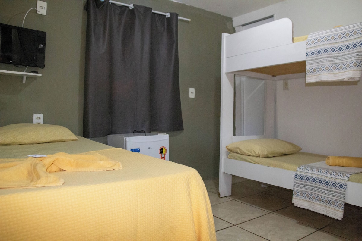 A room with a bunk bed, a single bed, a television mounted on the wall, and a small refrigerator.