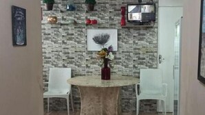 A dining area with a round table, two white chairs, a vase with flowers, a wall-mounted TV, and a framed picture. - Casa Aeroporto Pousada (Recife)