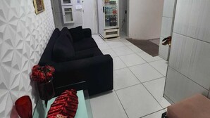 A modern living room with a black sofa, a glass coffee table with a red object, and a brown ottoman. - Casa Aeroporto Pousada (Recife)