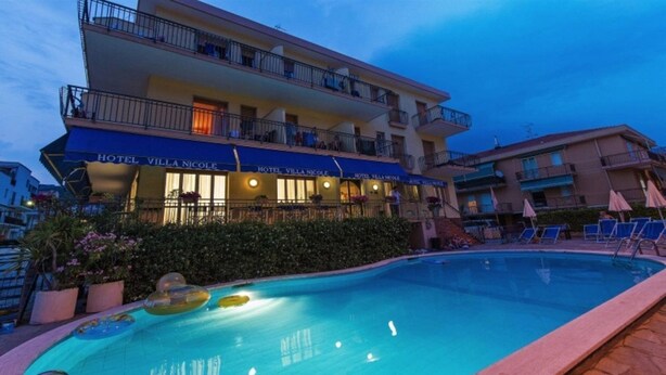 Un hotel con piscina, mobiliario exterior y fachada bien iluminada.