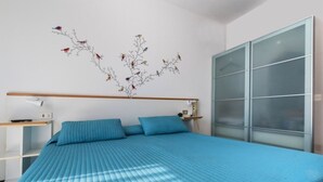 Un dormitorio con cama, mesita de noche, lámpara de pared y puerta corredera de cristal.
