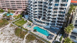 A high-rise hotel with multiple balconies, a swimming pool, and a landscaped area with palm trees.
