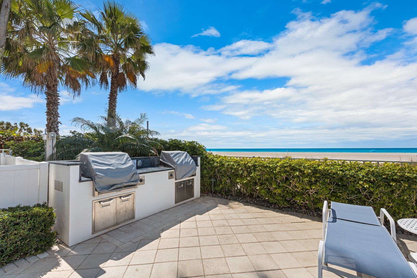 Un patio exterior con una parrilla, asientos y vistas a la playa.