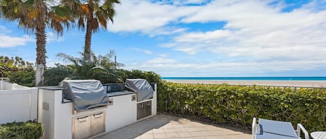 Un patio exterior con una parrilla, asientos y vistas a la playa.