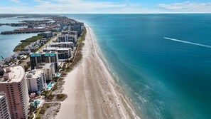 A coastal cityscape with a beachfront hotel, high-rise buildings, and a clear view of the ocean.
