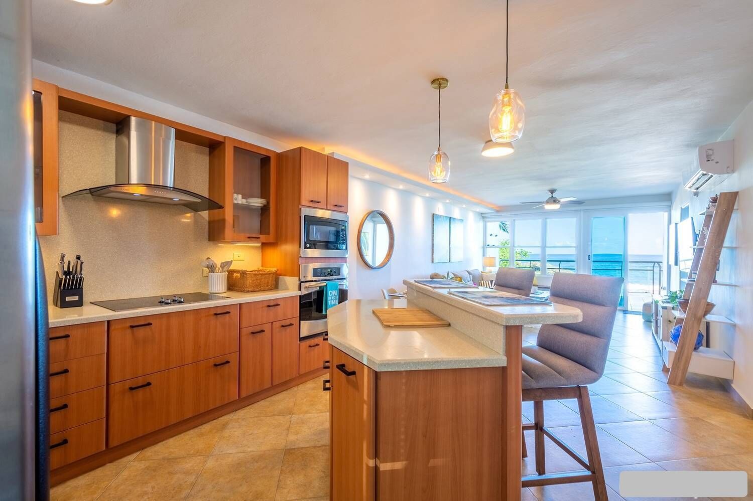 A modern kitchen with wooden cabinets, a stainless steel range hood, and a bar area with a view of the ocean.