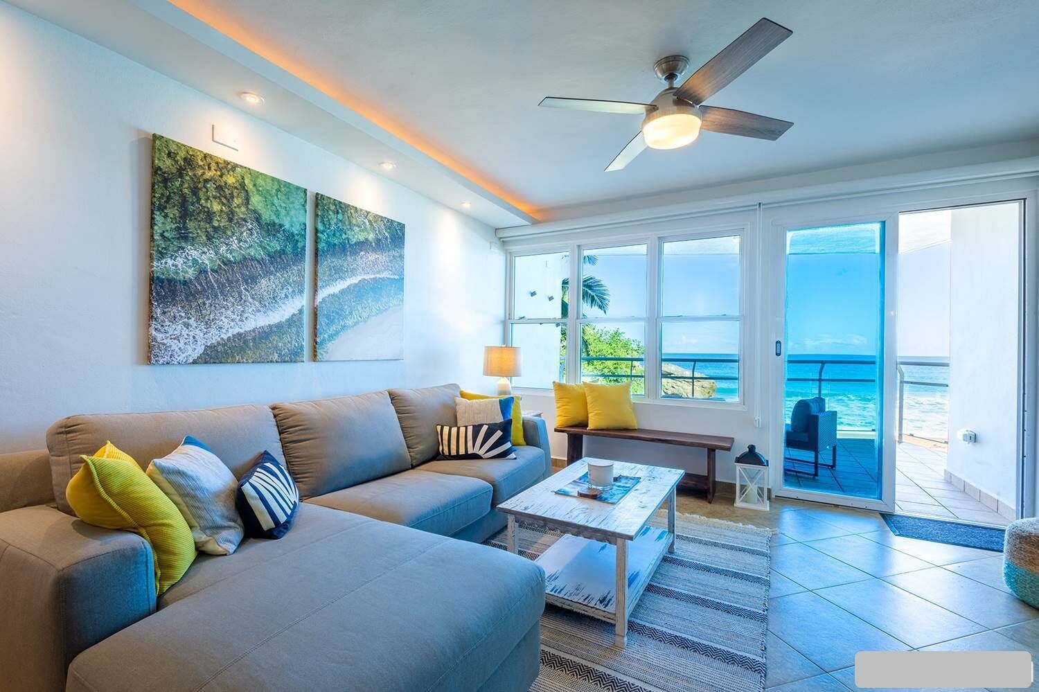 A living room with a sofa, coffee table, and a view of the ocean through large windows.