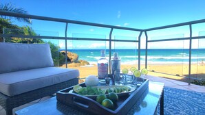 Un balcon donnant sur la plage, une table en verre avec un plateau de citrons verts, une bouteille de rhum argenté Rincón et un shaker à cocktails.