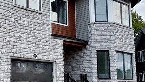Una casa moderna de dos pisos con fachada de piedra, un garaje y una escalera de metal negro.