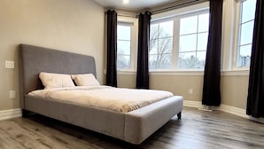 Un dormitorio con una cama grande, suelo de madera, una ventana con cortinas e iluminación en el techo.