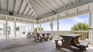 An outdoor covered patio with wooden tables and benches, white railings, and a view of palm trees.