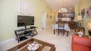 A living room with a television, a dining area with a table and chairs, and a kitchen in the background.