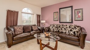 A living room with two brown leather sofas, a glass coffee table, and a pink wall with framed artwork. - Aviana Resort-ru1077 (Davenport)