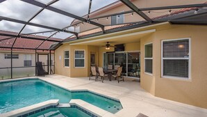 A covered outdoor swimming pool area with a ceiling fan, a table with chairs, and a view of neighboring buildings. - Aviana Resort-ru1077 (Davenport)