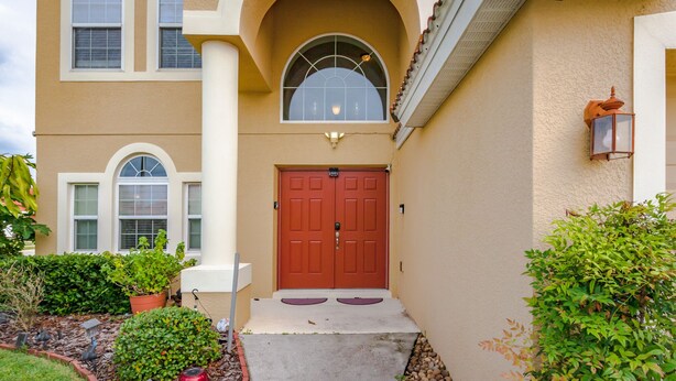 A two-story building with a red door, a small porch, and a garden with potted plants and a pathway. - Aviana Resort-ru1077 (Davenport)