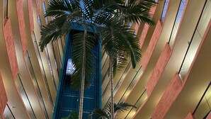 A modern building with a central atrium, multiple floors, and a tall palm tree.