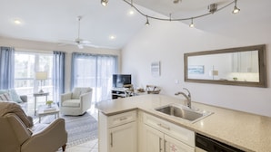 A modern kitchen with a central island, a dining area with a sofa and chairs, a television, and a large mirror. - Gulf view, Pool, Deed Beach Beach Access in Santa Rosa Beach.  (Santa Rosa Beach)