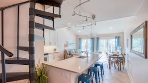 A modern kitchen with a central island, a staircase, and a dining area with blue bar stools. - Gulf view, Pool, Deed Beach Beach Access in Santa Rosa Beach.  (Santa Rosa Beach)