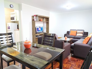 A modern living room with a glass dining table, a sofa set, and a television. - Eral Apartments Country Club (Lima)