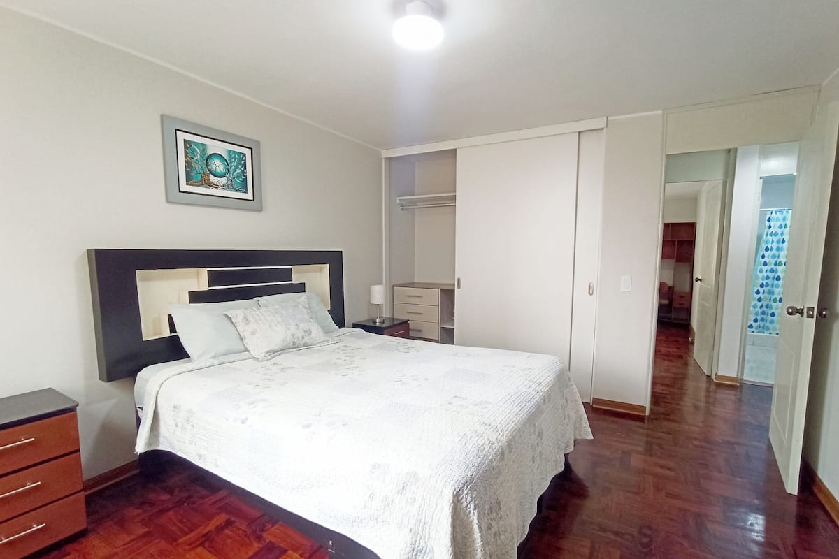 Ein Schlafzimmer mit Bett, Nachttisch, Kommode und begehbarem Kleiderschrank.