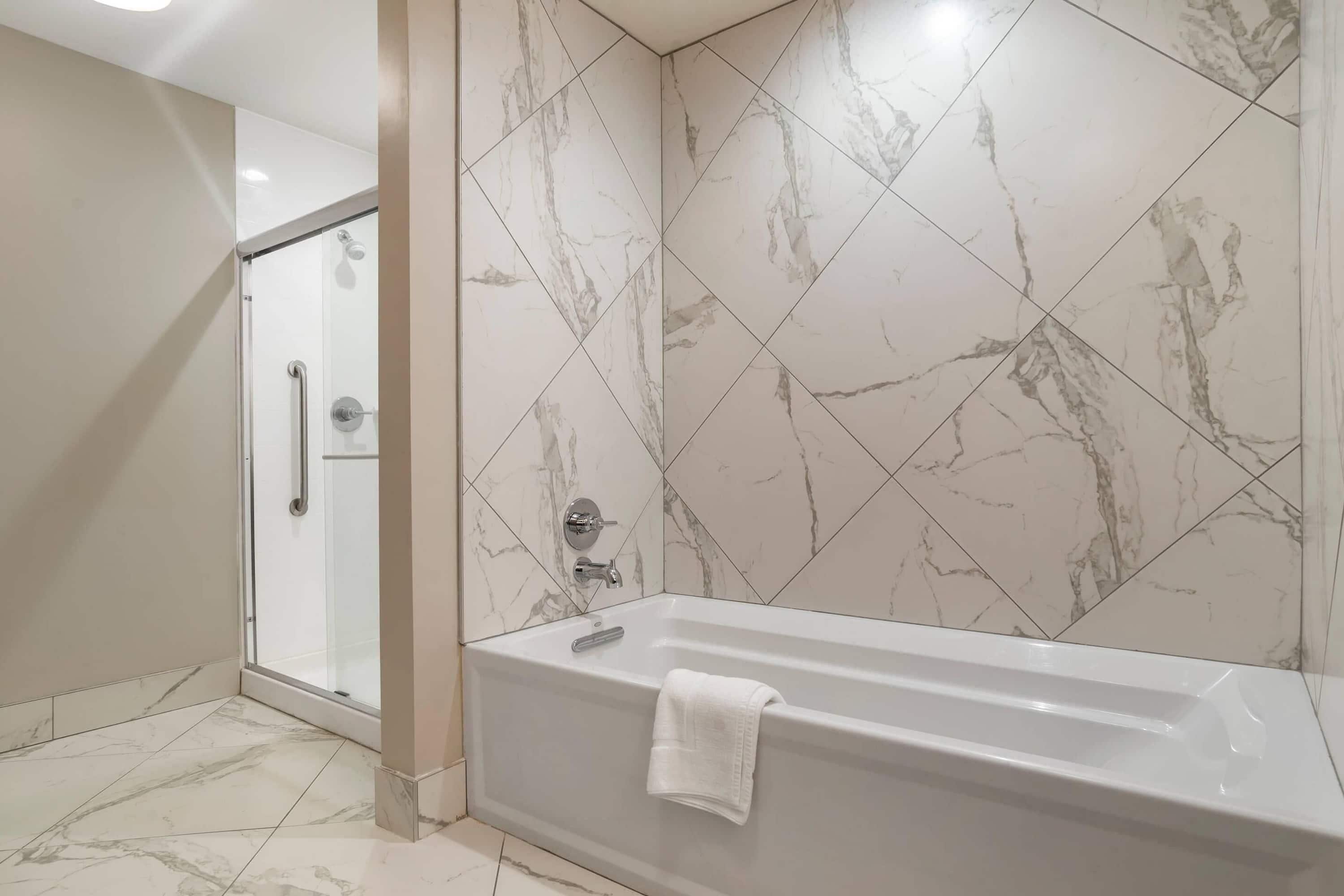 Une salle de bain moderne dotée d’une douche à l’italienne, d’une baignoire et de murs aux motifs de marbre.