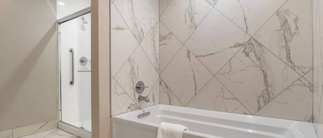 Une salle de bain moderne dotée d’une douche à l’italienne, d’une baignoire et de murs aux motifs de marbre.