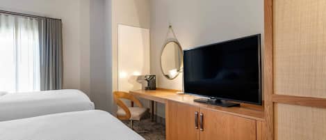 A hotel room with two beds, a TV, a desk with a chair, and a mirror.