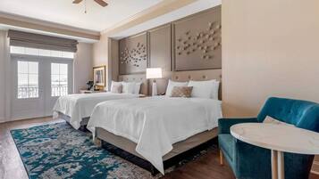 A hotel room with two beds, a blue armchair, a small round table, and a ceiling fan.