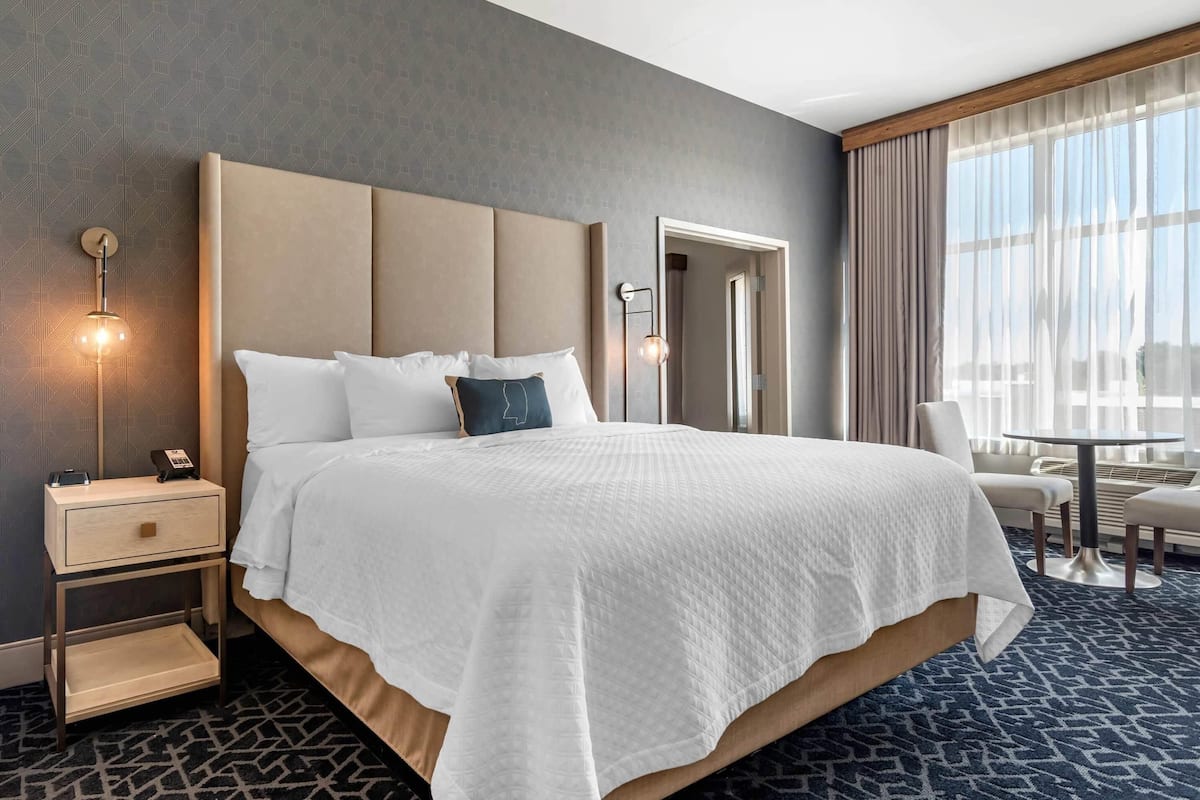A hotel room with a large bed, bedside tables, a desk, and a view of the outdoors.